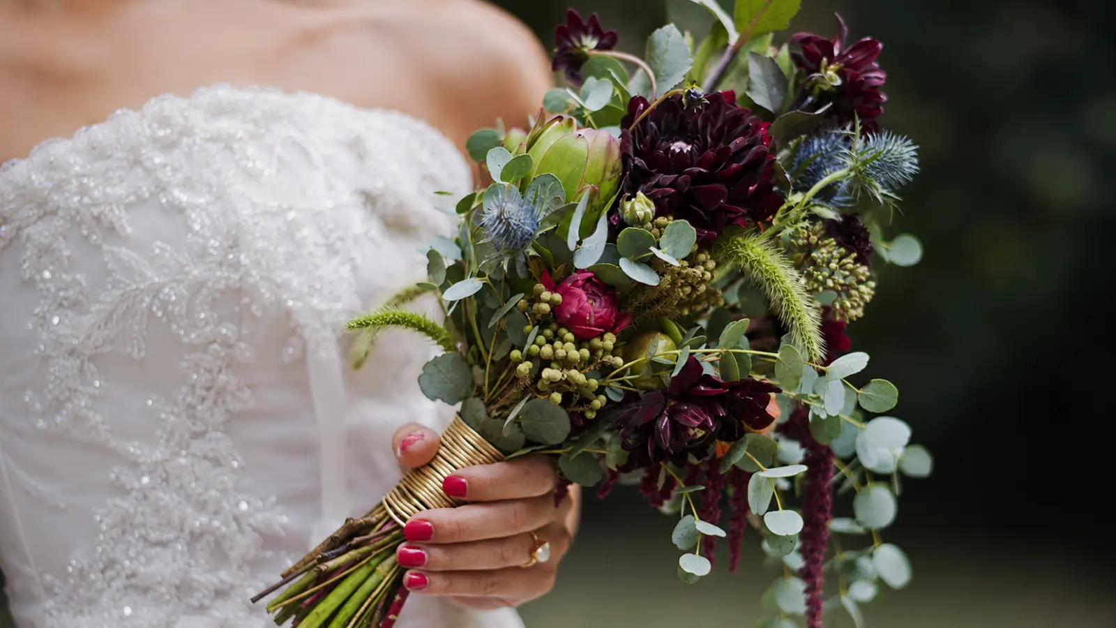 Bride holding a moody winter wedding bouquet with dark flowers, eucalyptus, berries and seasonal greenery