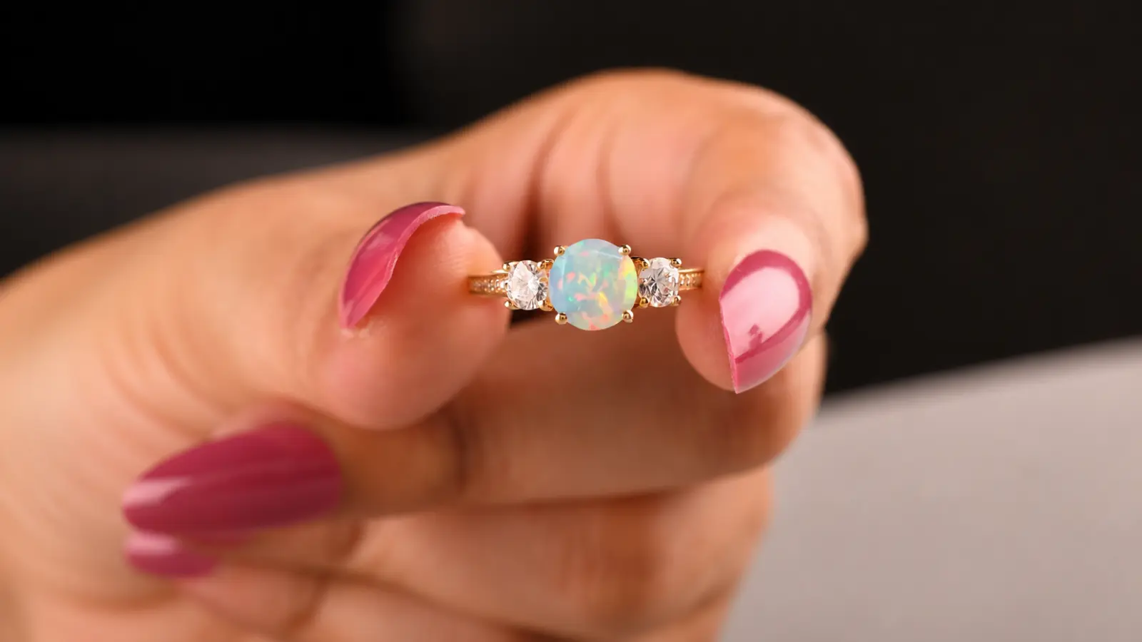 An opal and diamond three-stone engagement ring is held between fingers, showcasing a luminous opal center flanked by two sparkling round diamonds