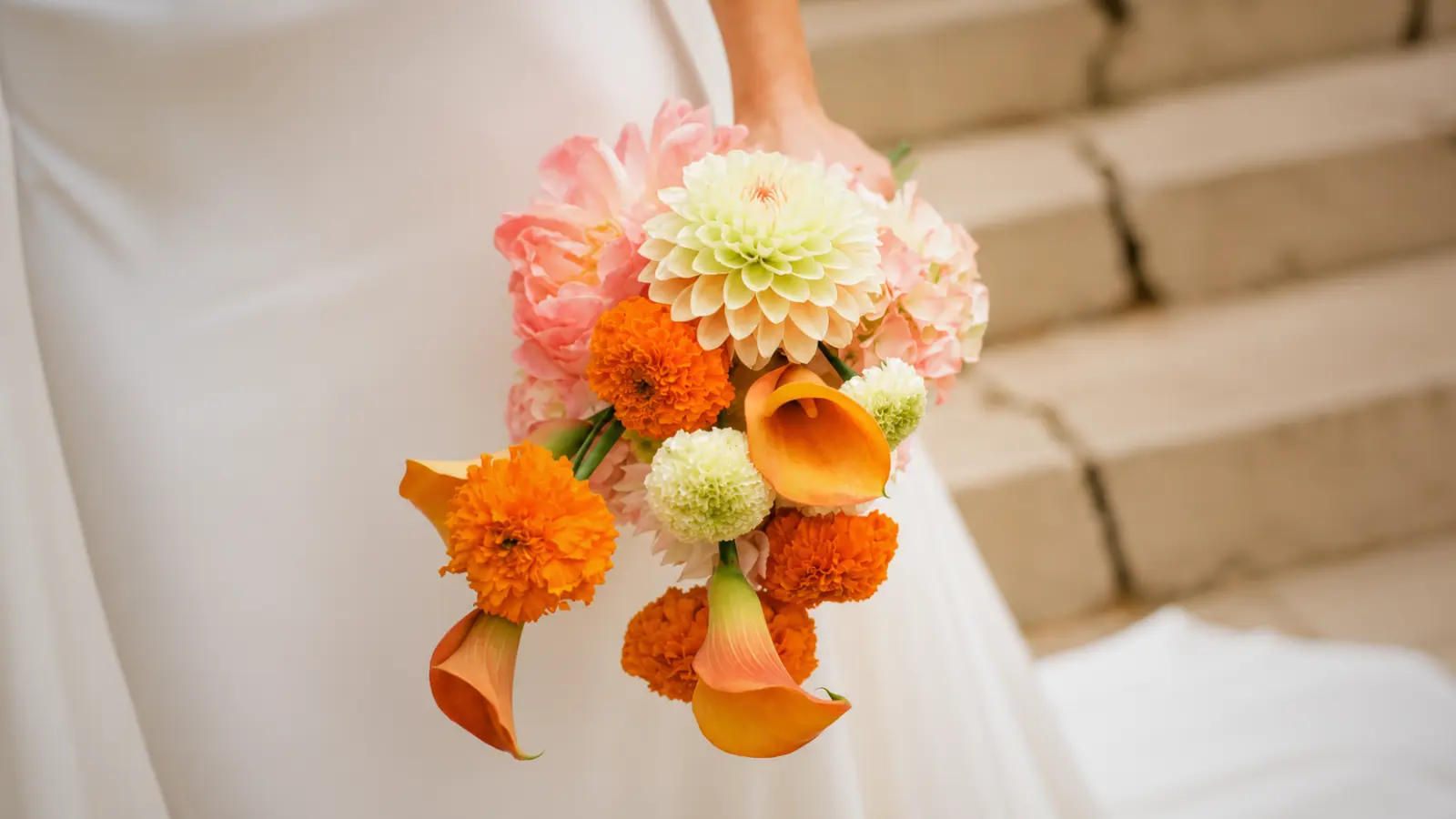 Bride holding an orange and blush wedding bouquet with calla lilies and dahlias