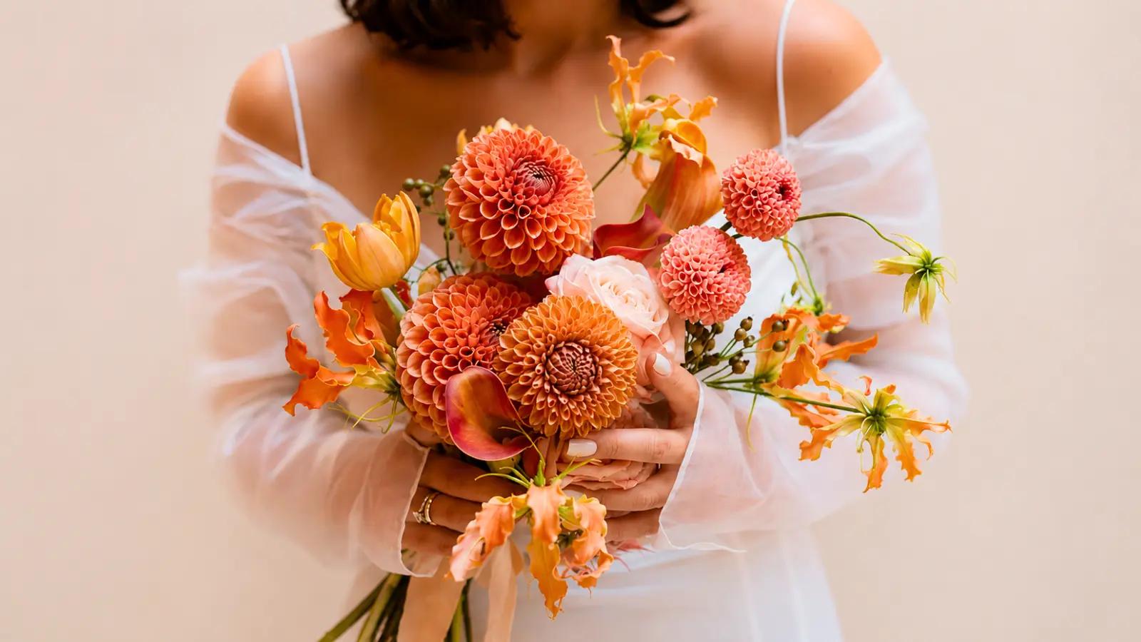 Bride holding a colorful wedding bouquet featuring orange dahlia wedding bouquets, roses, calla lilies, and seasonal flowers