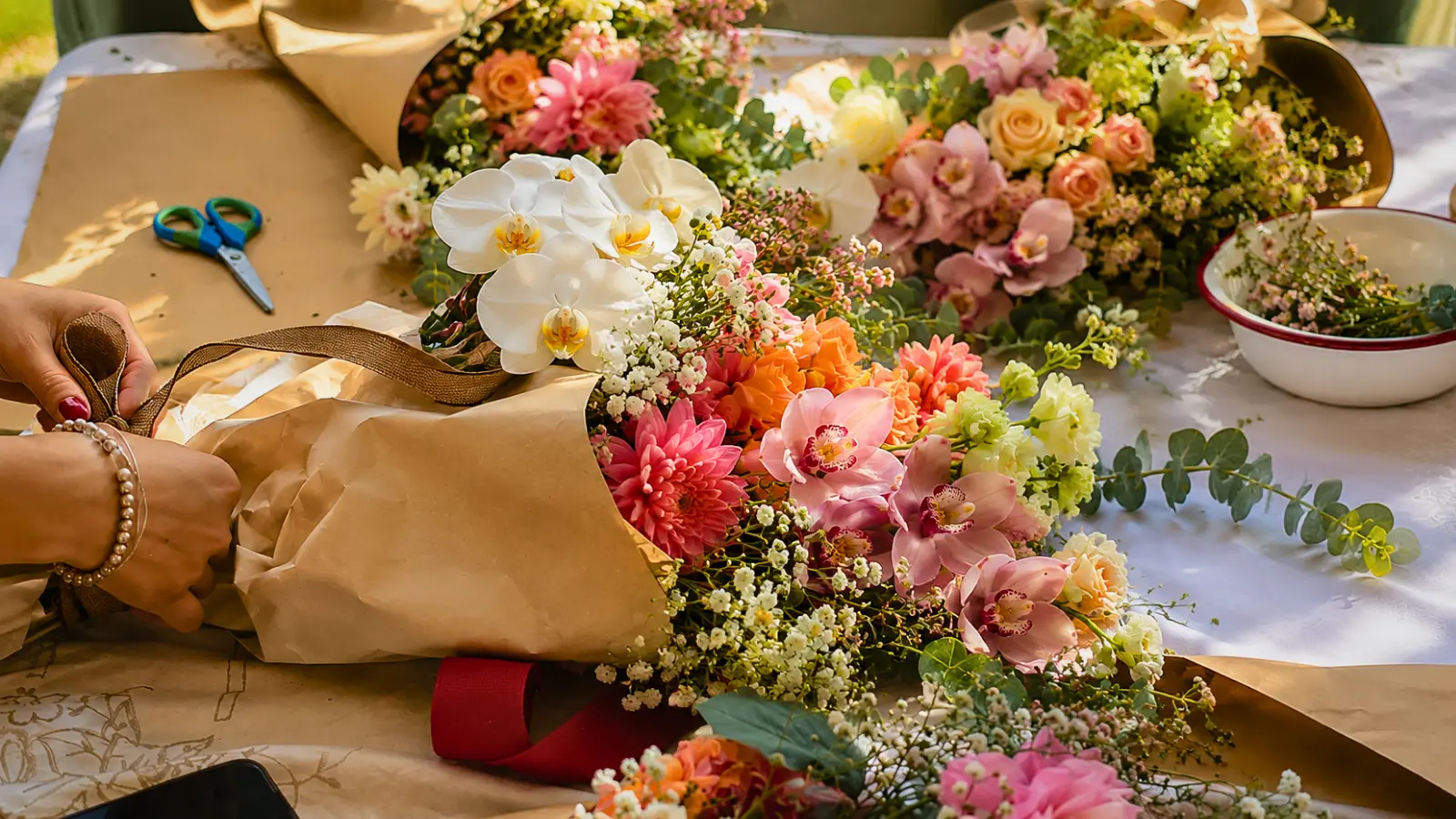 Florist wrapping a wedding bouquet with white orchids, pink orchids, roses, eucalyptus, and fresh seasonal flowers