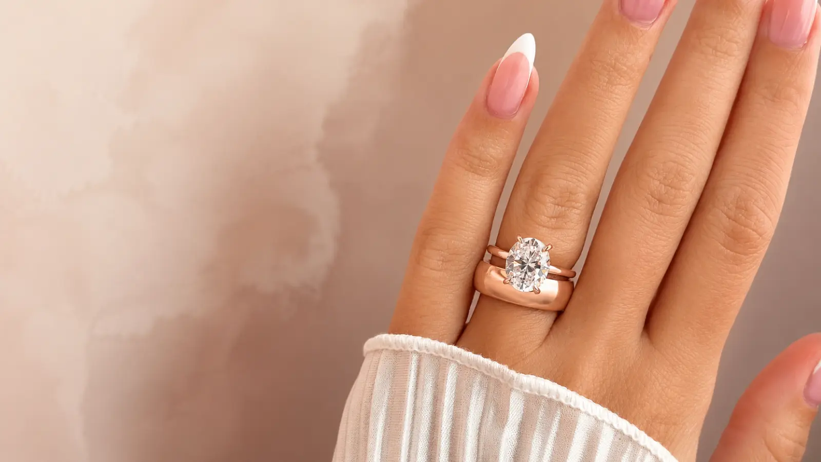A bride wears an oval diamond engagement ring stacked with a polished rose gold wedding band, highlighting the warm metal tone and sophisticated layered bridal style