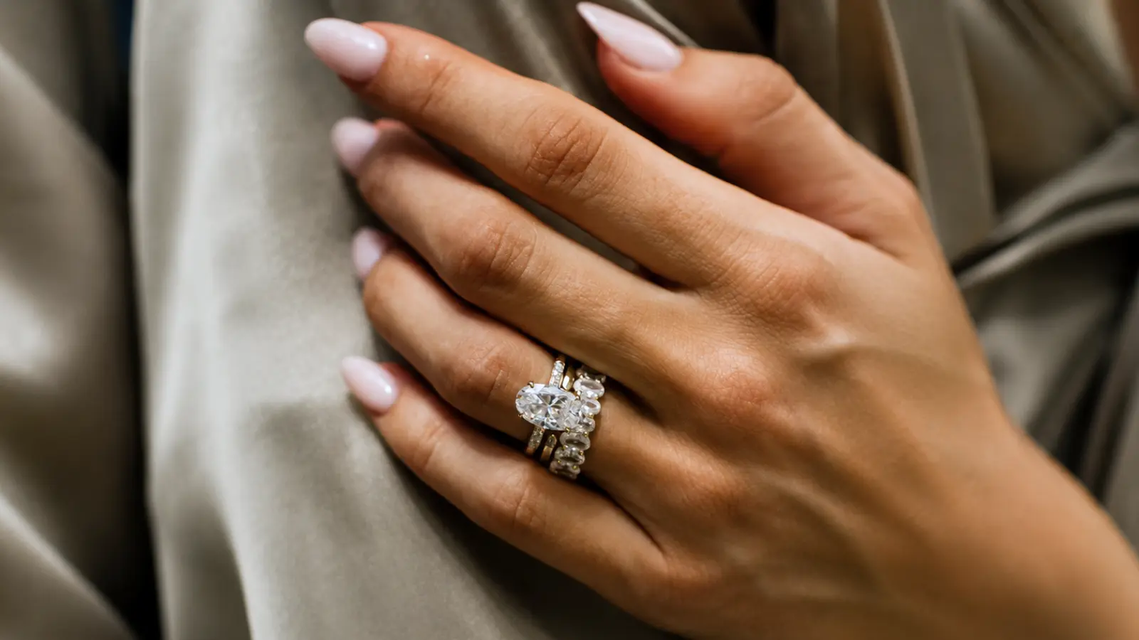 An oval engagement ring surrounded by matching wedding bands in a coordinated bridal stack on a woman's hand