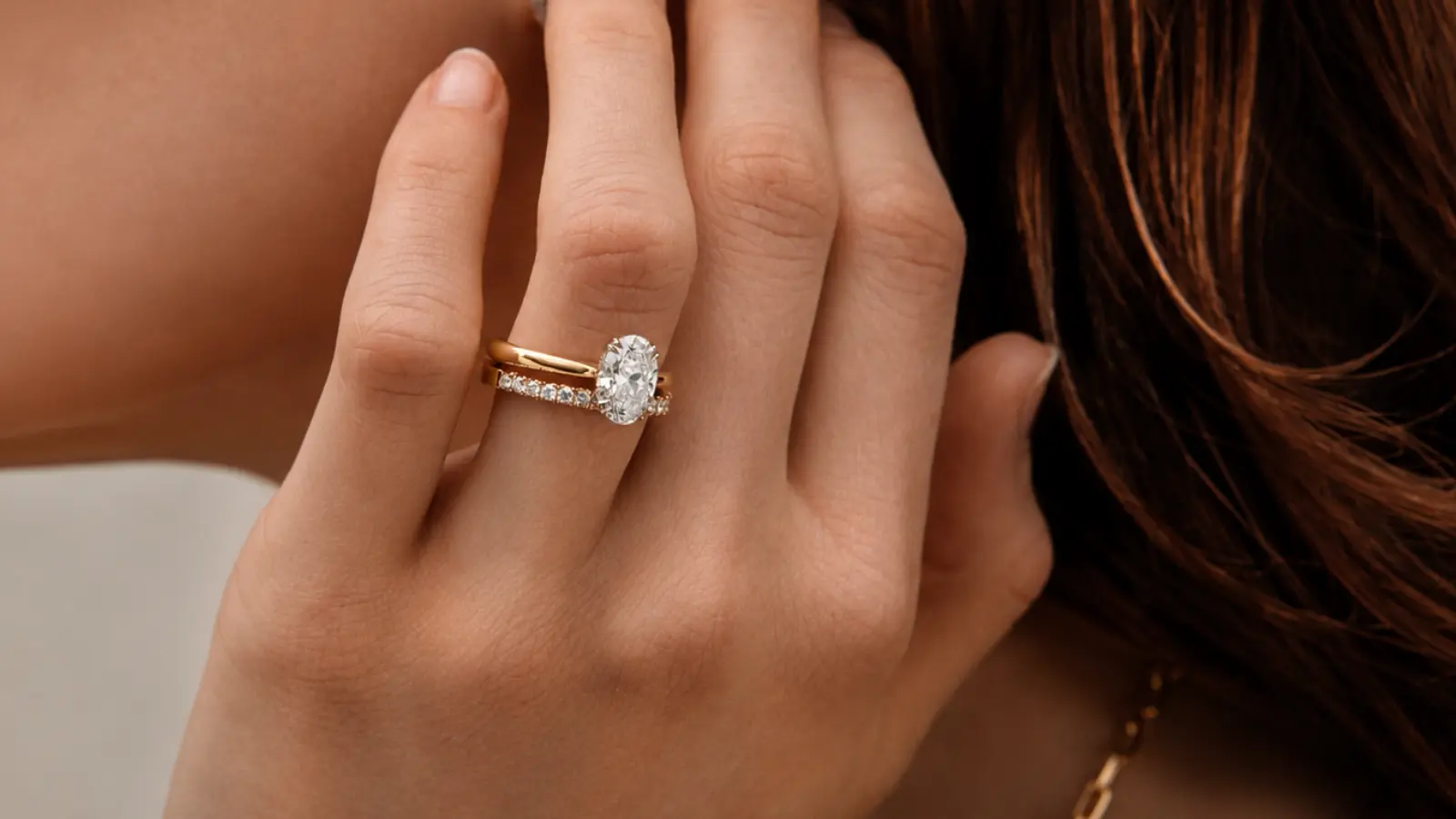 An oval engagement ring paired with a thin pavé diamond wedding band on a woman's hand