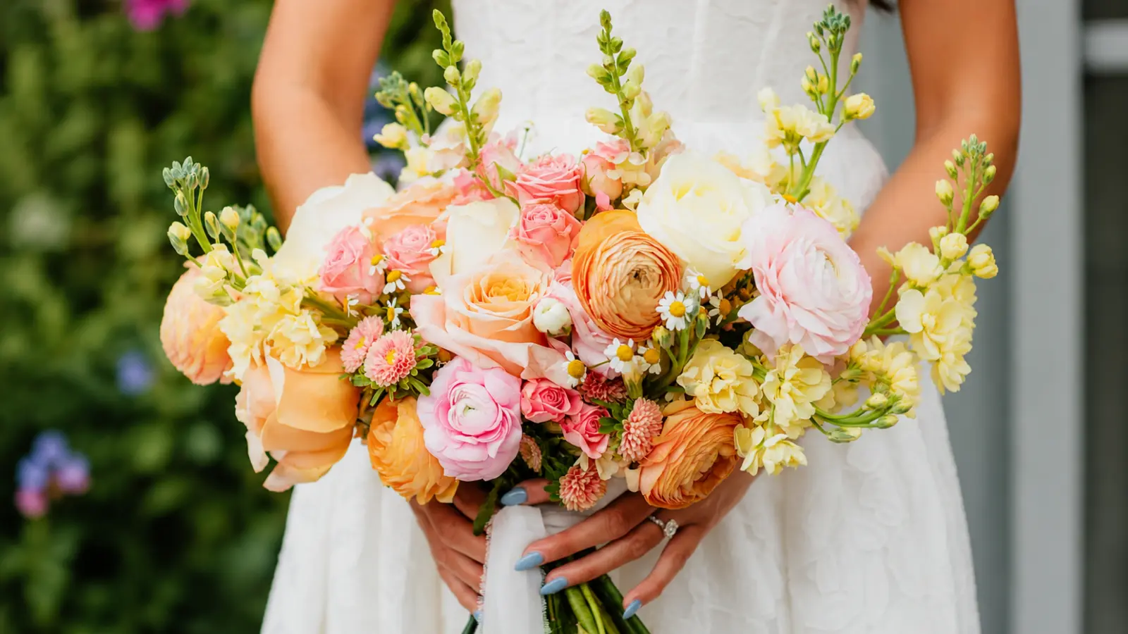 Bride holding a pastel colorful wedding bouquet with garden roses, ranunculus and spring flowers
