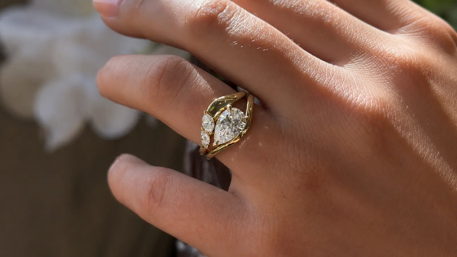 A pear-shaped diamond engagement ring framed by a yellow gold wedding ring wrap with matching side diamonds on a woman's hand