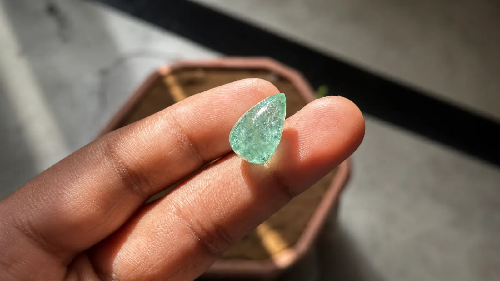 A pear-shaped natural emerald gemstone is held between fingertips, revealing its vivid green color and natural internal inclusions