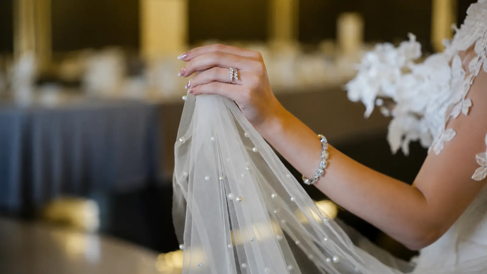 Bride holding a soft tulle wedding veil decorated with scattered pearl embellishments and elegant drape