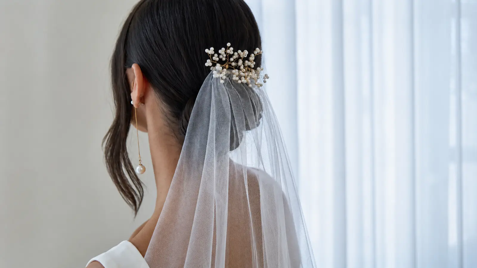 Bride wearing a low bridal hairstyle with a pearl hairpiece and a softly draped wedding veil Wedding Hairstyles With Veil