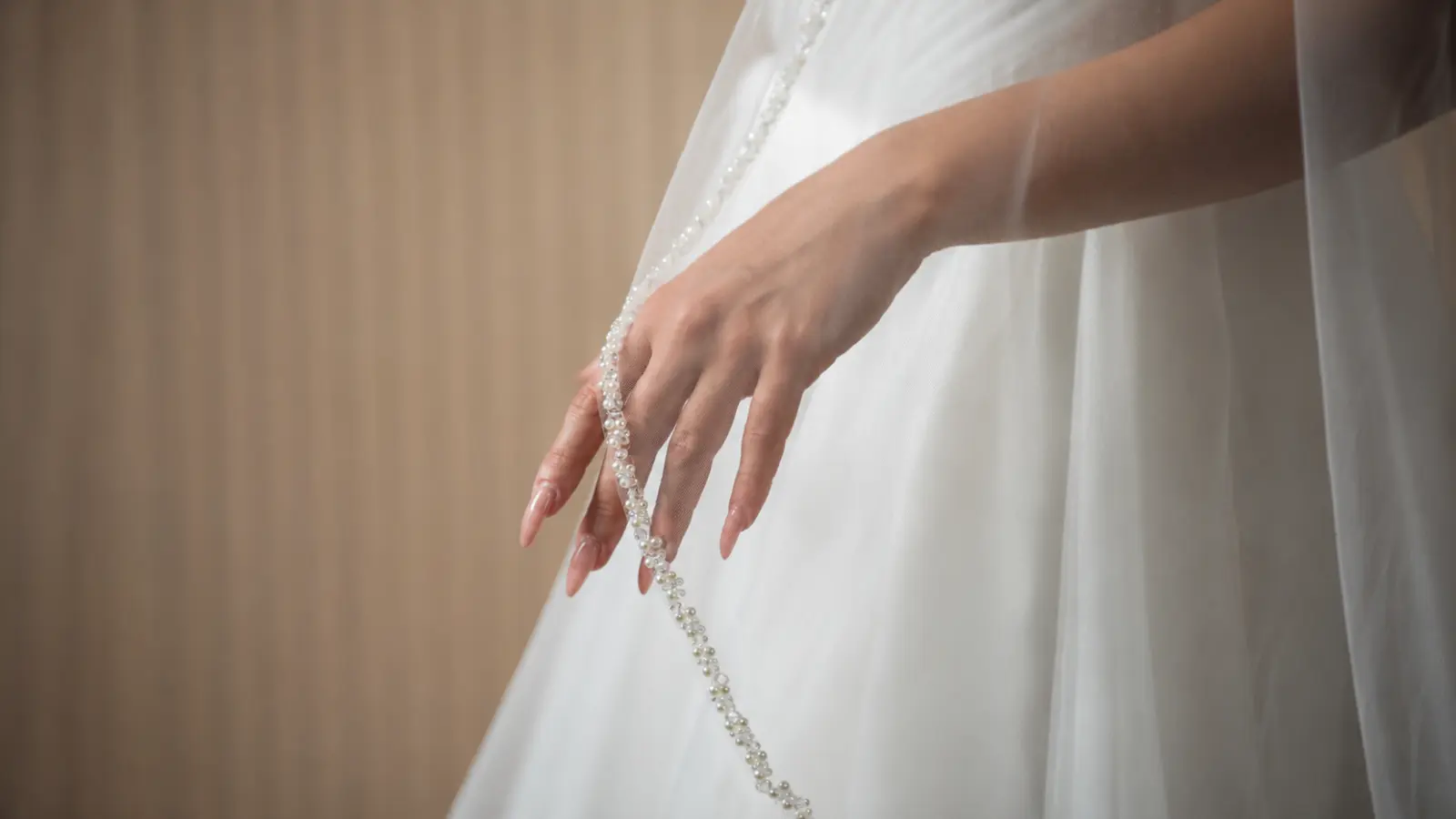 Close-up of a wedding veil with pearl trim draped beside a bridal gown, highlighting elegant detailing, soft tulle, and timeless bridal sophistication