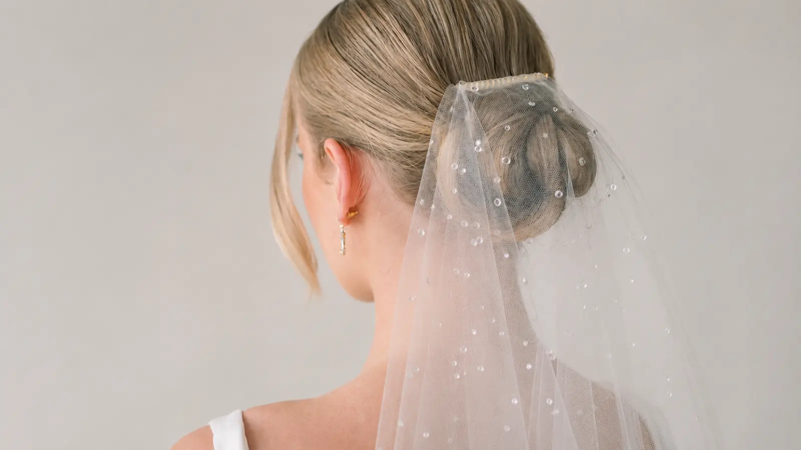 Back view of a bride wearing a pearl wedding veil attached above a polished low bun hairstyle