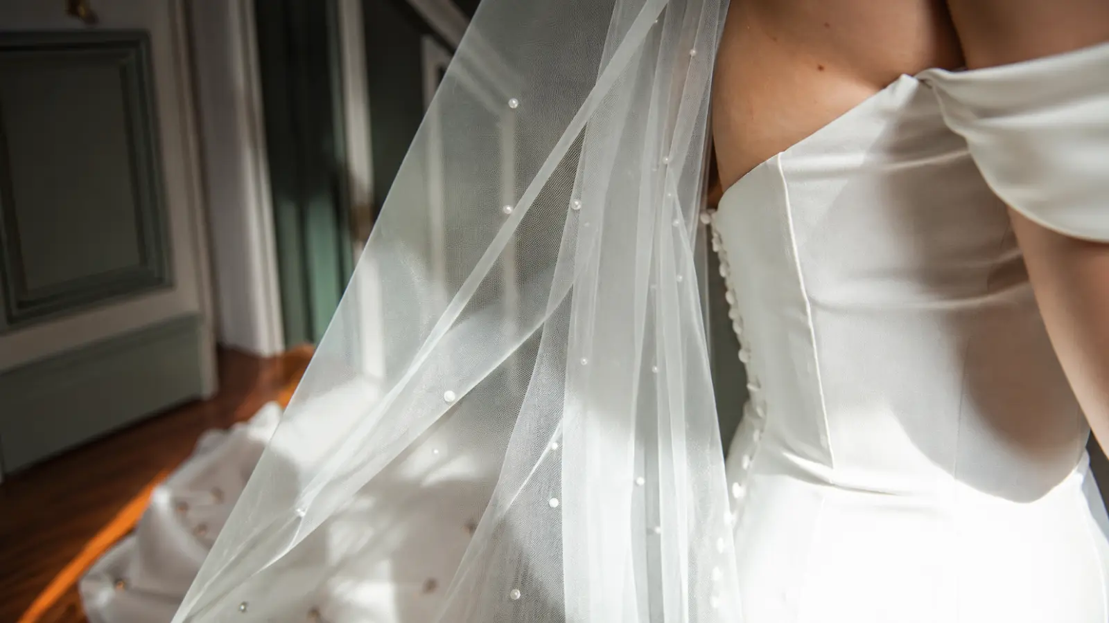 Close-up of a pearl wedding veil with illusion tulle and scattered pearl embellishments beside a satin wedding dress
