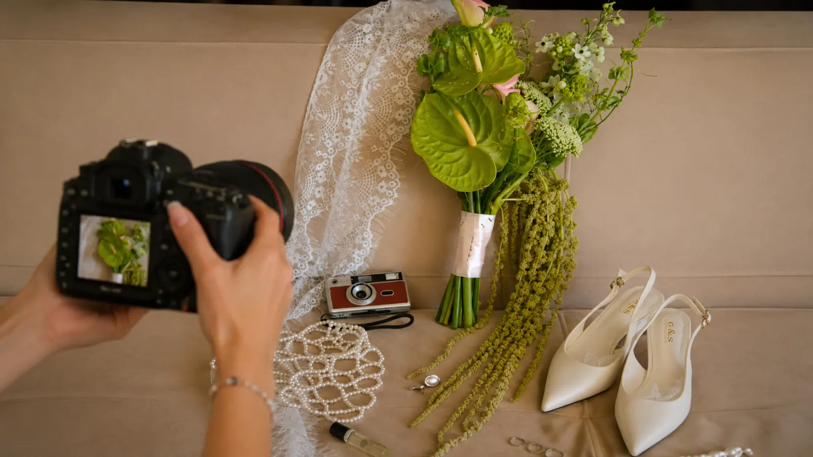 Photographer taking pictures of a green wedding bouquet with bridal shoes and wedding details