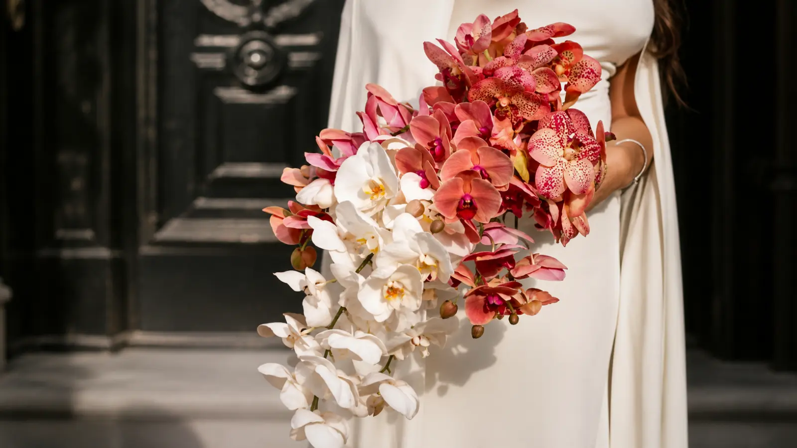 Bride holding a pink and white orchid cascading wedding bouquet with flowing orchids in soft romantic shades