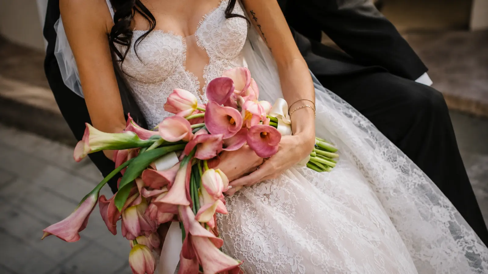 Bride holding a pink calla lily cascading wedding bouquet with soft cascading blooms while seated with the groom
