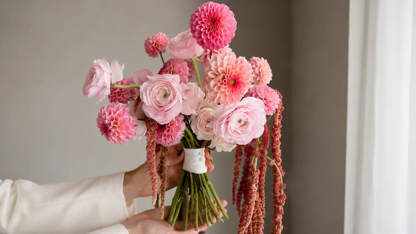Romantic bridal bouquet featuring pink dahlias, ranunculus, and cascading amaranthus stems