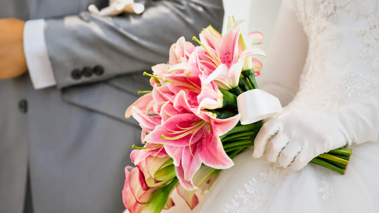 Bride seated beside the groom holding a bouquet of pink Stargazer lilies wrapped with a white satin ribbon