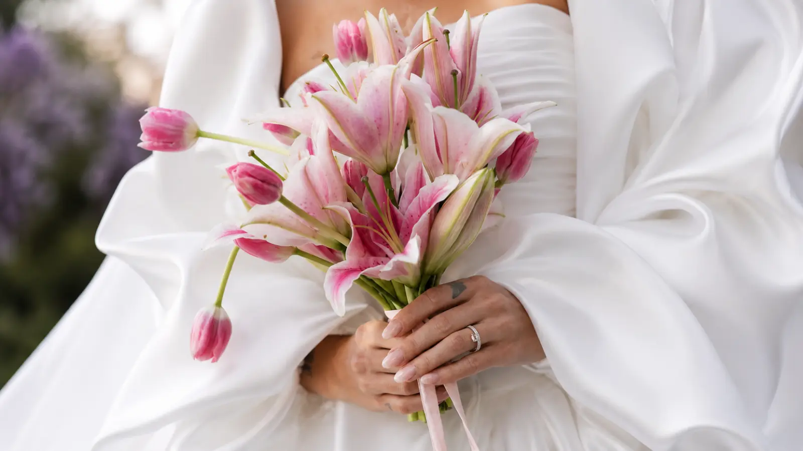 Bride holding a pink lily wedding bouquet accented with soft pink tulips and a satin ribbon