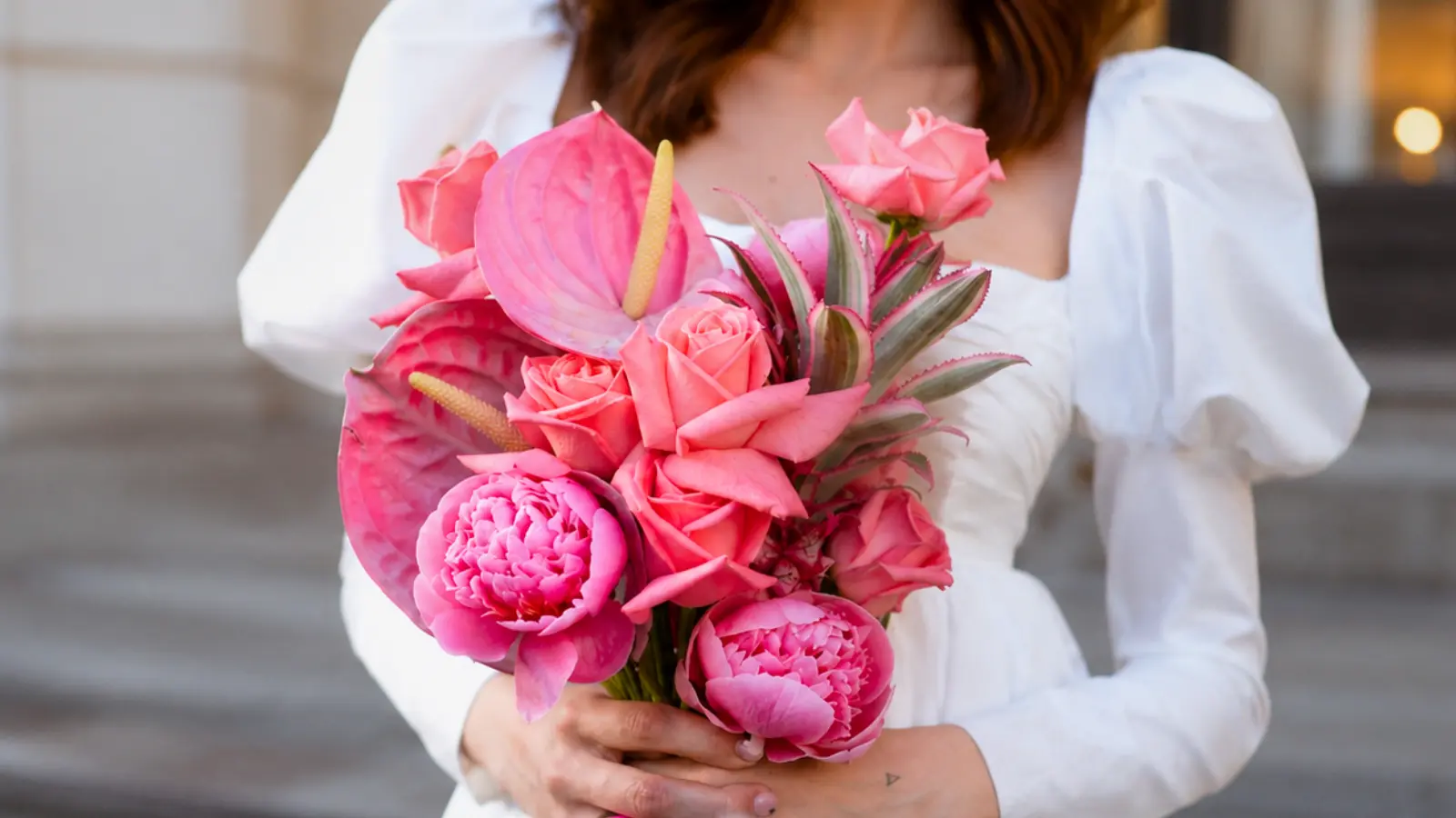 Bride holding a modern pink rose wedding bouquet featuring roses peonies and tropical flowers in vibrant shades