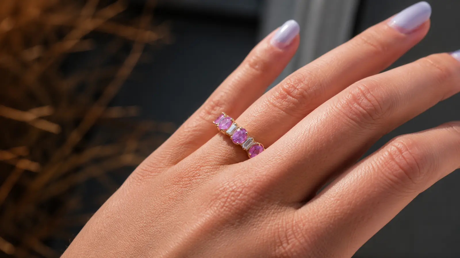 A close-up of a pink sapphire eternity wedding band with alternating pink sapphires and white gemstones worn on a woman's finger