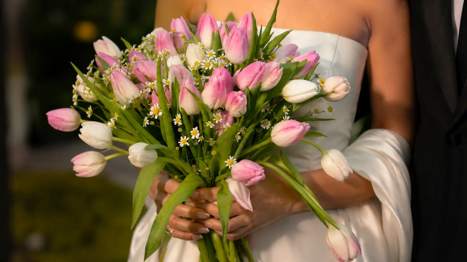 Bride holding a lush bouquet of pink and white tulips with delicate chamomile flowers