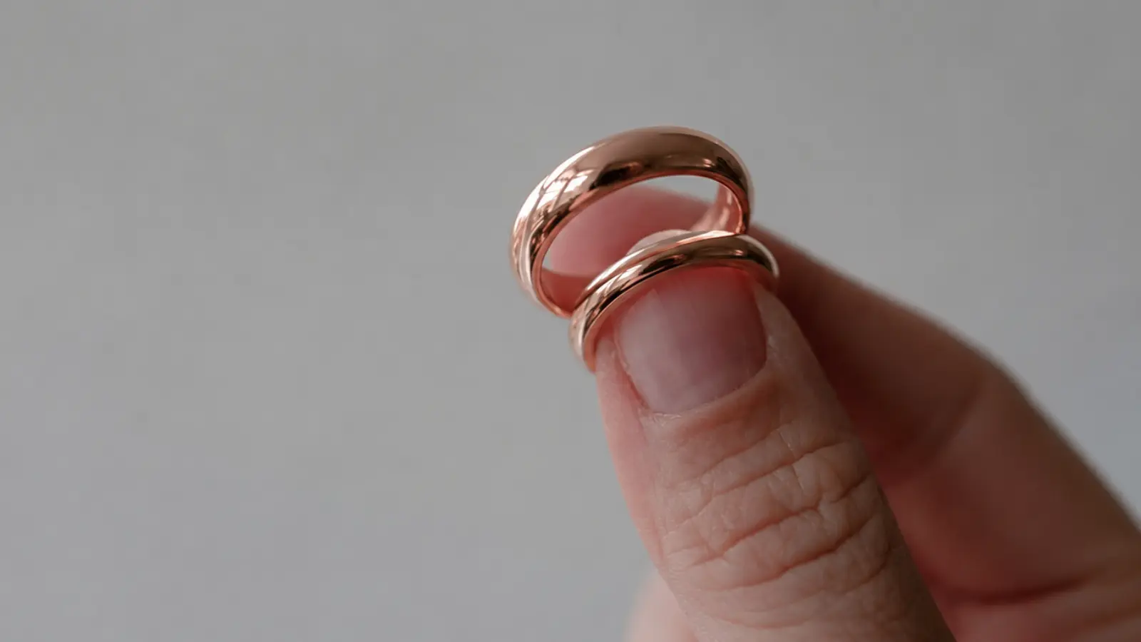 Two polished rose gold wedding rings are held between fingers, highlighting their rounded shape, reflective finish and distinctive warm blush tone in a detailed close-up Rose Gold Wedding Rings