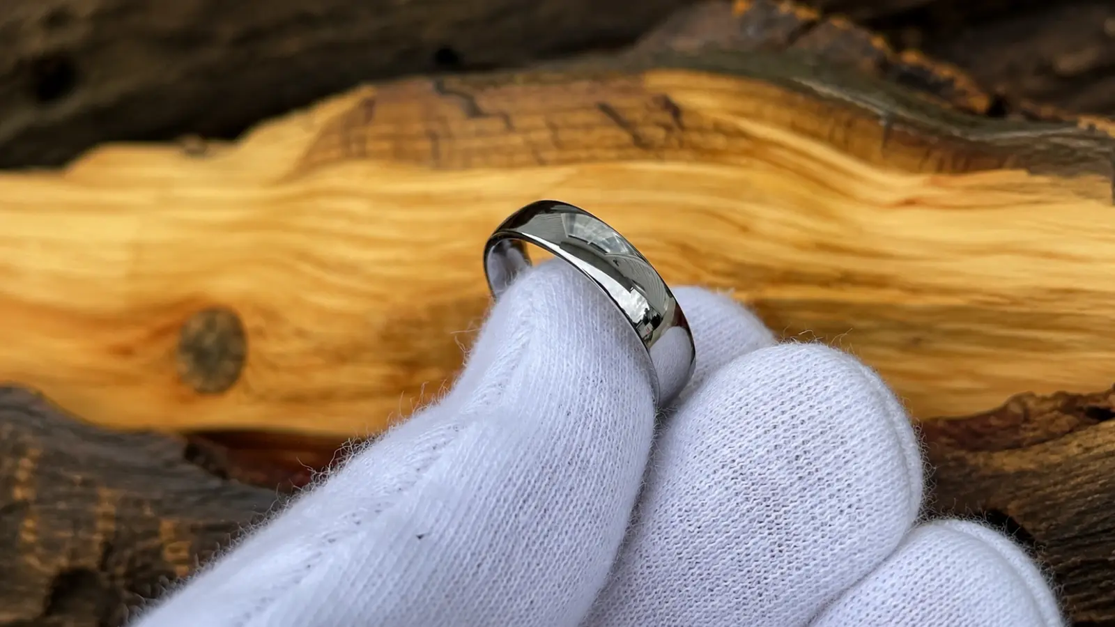 A polished titanium wedding ring is held with a white glove, highlighting its reflective finish, minimalist design and durable metal construction