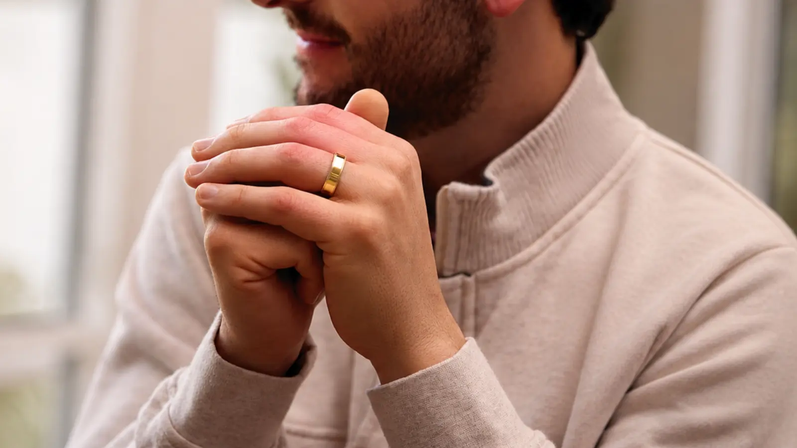 Man wearing a polished yellow gold men's wedding ring with a light neutral sweater, showing how a classic gold wedding band complements casual outfits