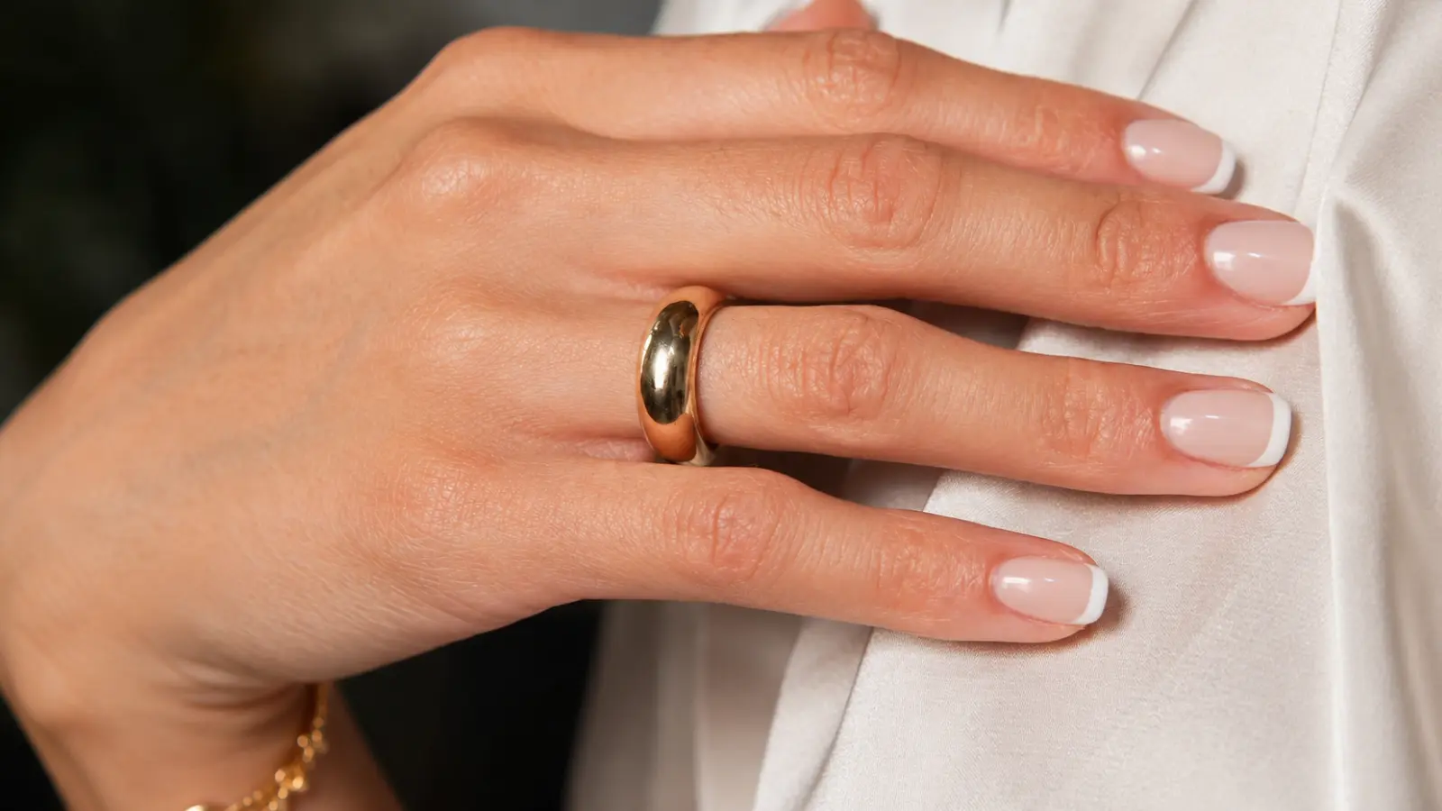 A polished yellow gold wedding ring rests on a bride's finger with a classic French manicure, emphasizing the warm color, smooth finish and enduring elegance of a traditional wedding band