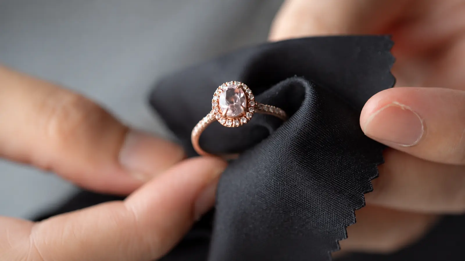 A halo engagement ring being polished with a black microfiber cloth to safely remove fingerprints and restore shine