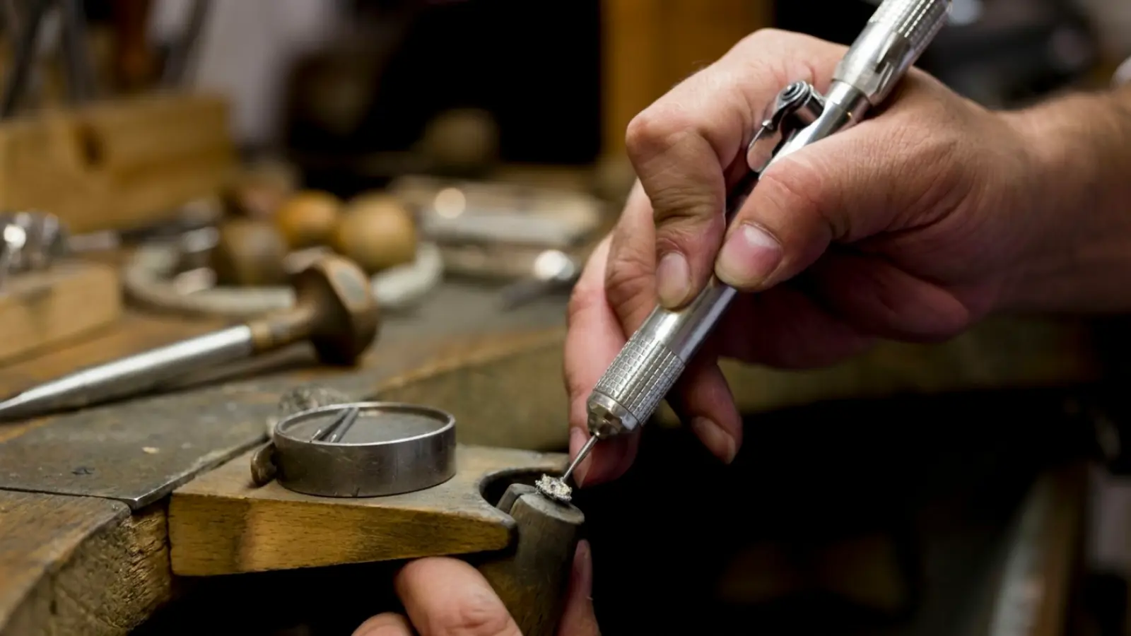 A professional jeweler using a precision engraving and setting tool to perform delicate adjustments on a diamond engagement ring during a wedding ring upgrade and fine jewelry restoration process