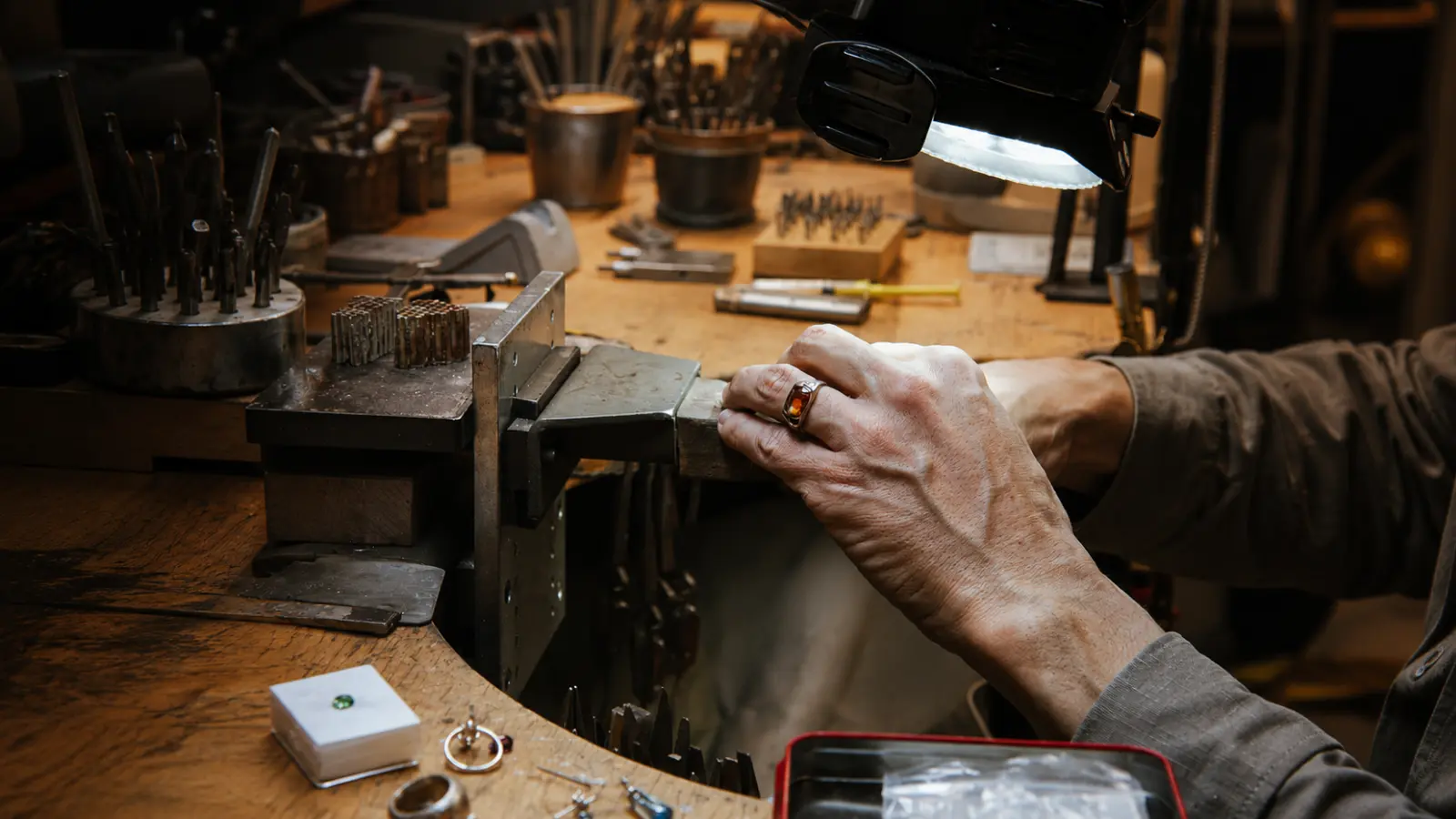 A jeweler working at a professional jewelry bench equipped with specialized tools used for wedding ring resizing and repairs