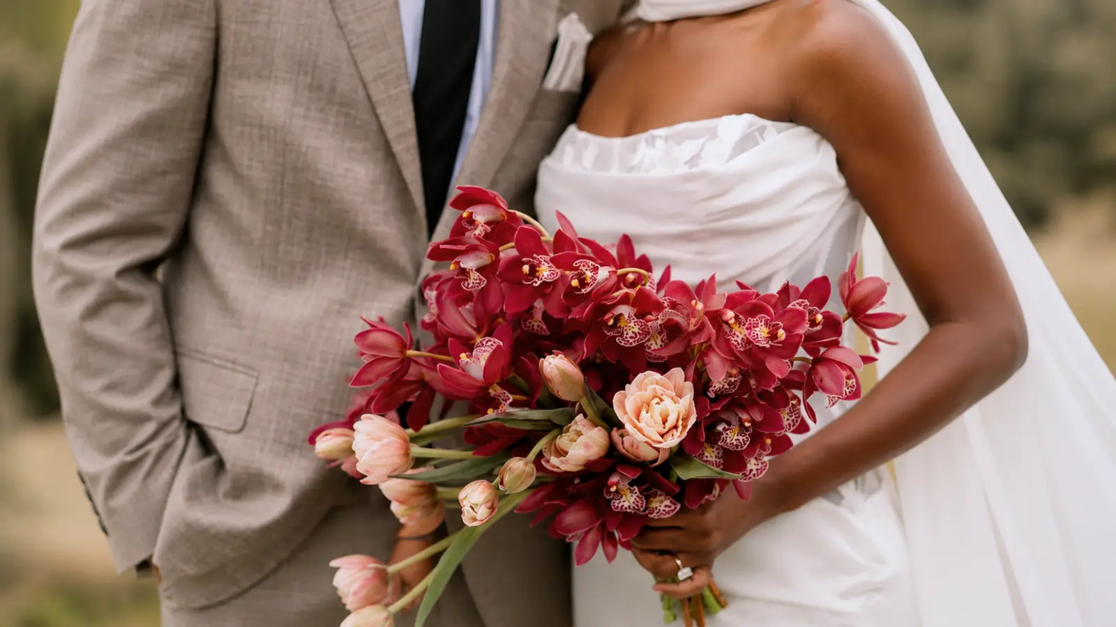 Bride holding a vibrant red cymbidium orchid wedding bouquet with blush tulips and garden roses