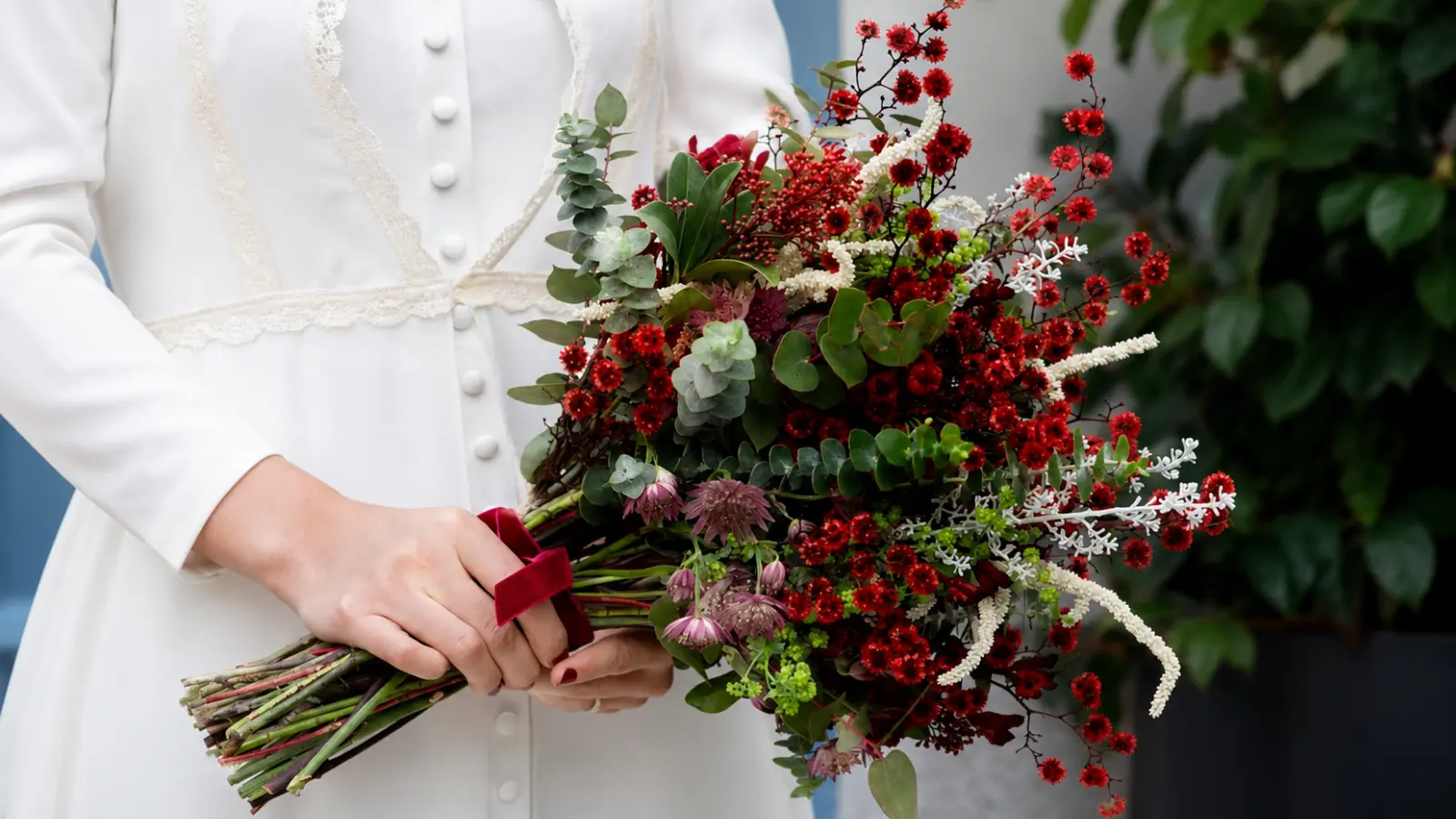 Bride holding a red winter wedding bouquet with eucalyptus, waxflowers and textured seasonal greenery
