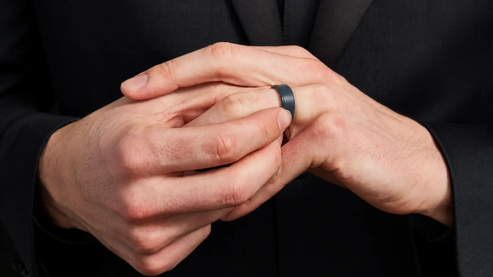 Man placing a black silicone wedding band onto his finger while wearing a dark suit
