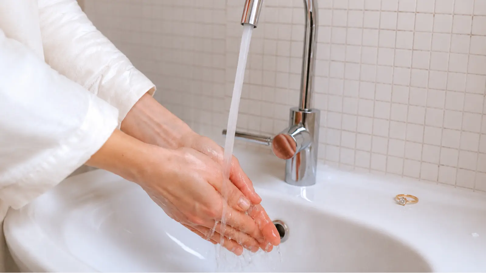 Hands being rinsed under running water after cleaning a wedding ring during a safe at-home jewelry care routine