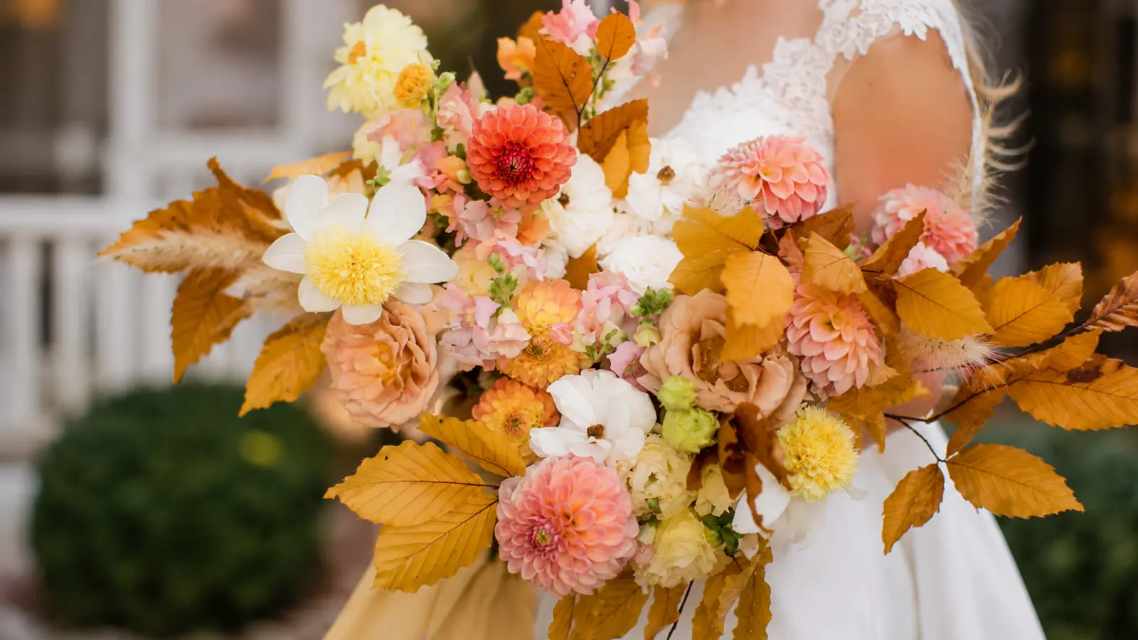 Bride holding a romantic fall wedding bouquet with pastel blooms and colorful autumn leaves
