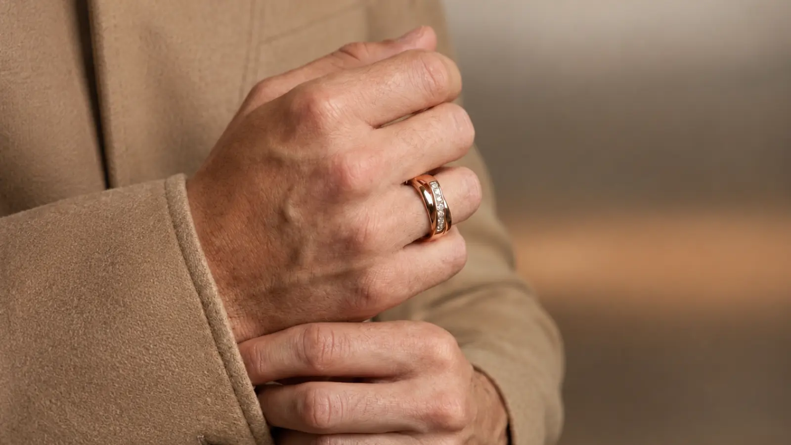 Man wearing a rose gold men's diamond wedding band featuring a row of channel-set diamonds with a tailored beige coat Men's Diamond Wedding Bands