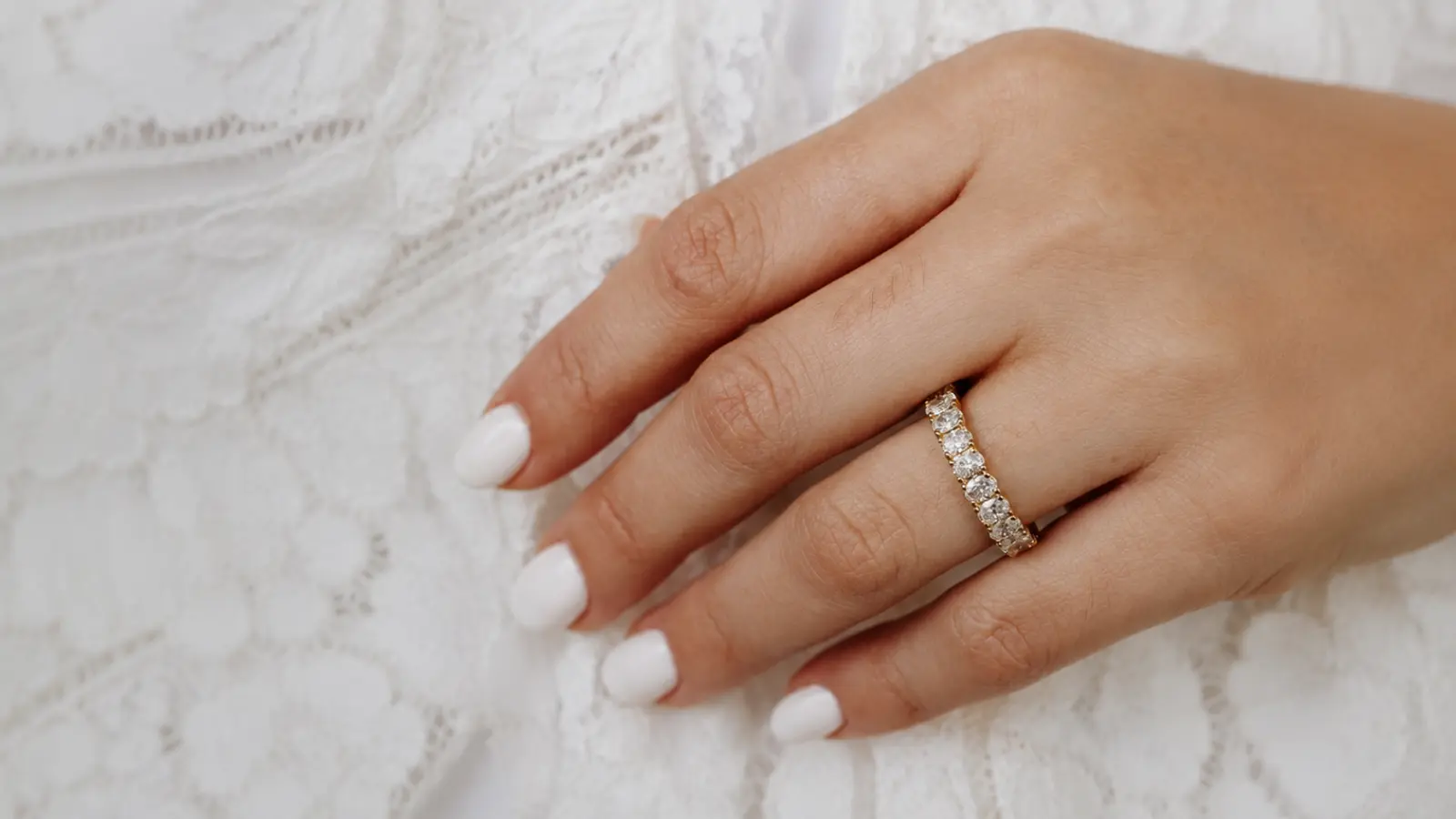 A hand wearing a round diamond eternity wedding band showcases a full circle of brilliant diamonds set in polished yellow gold