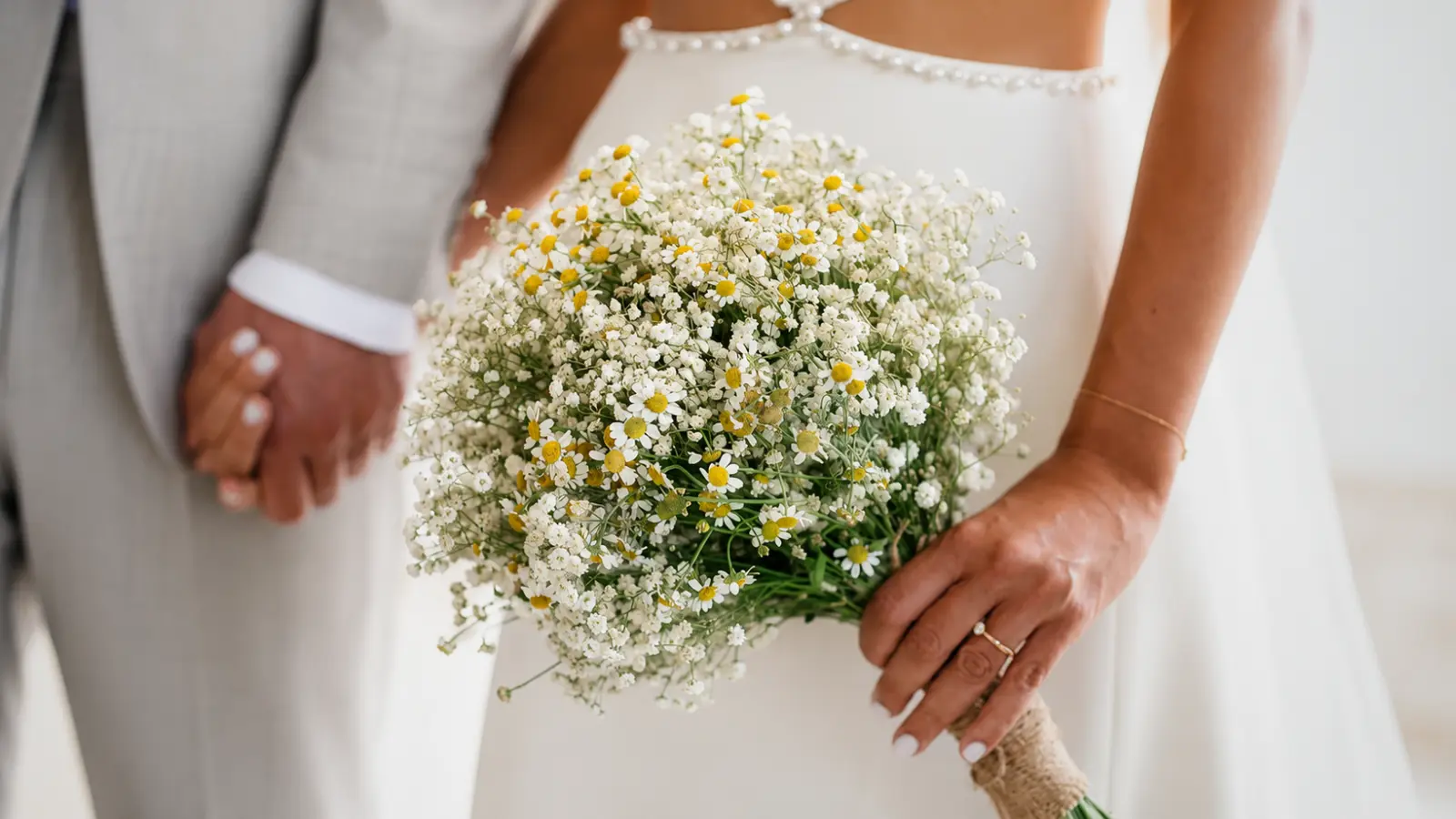 Bride holding a rustic baby's breath wedding bouquet accented with small white daisy flowers
