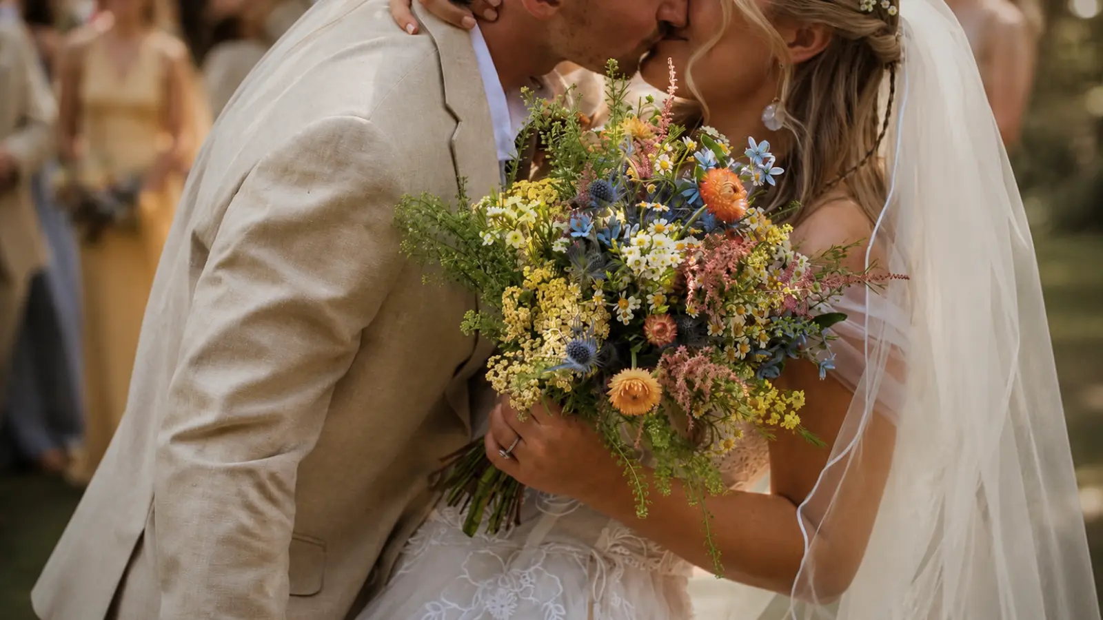 Couple kissing while holding a rustic wedding bouquet with colorful wildflowers