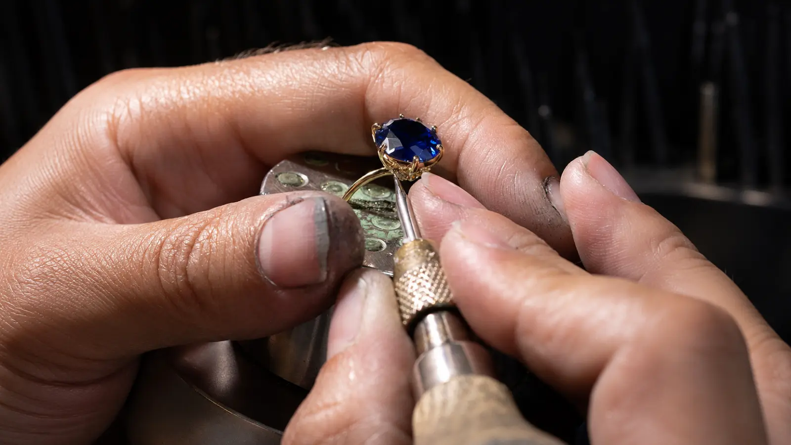 A jeweler carefully sets a deep blue sapphire gemstone into a gold ring using precision tools at a professional workbench