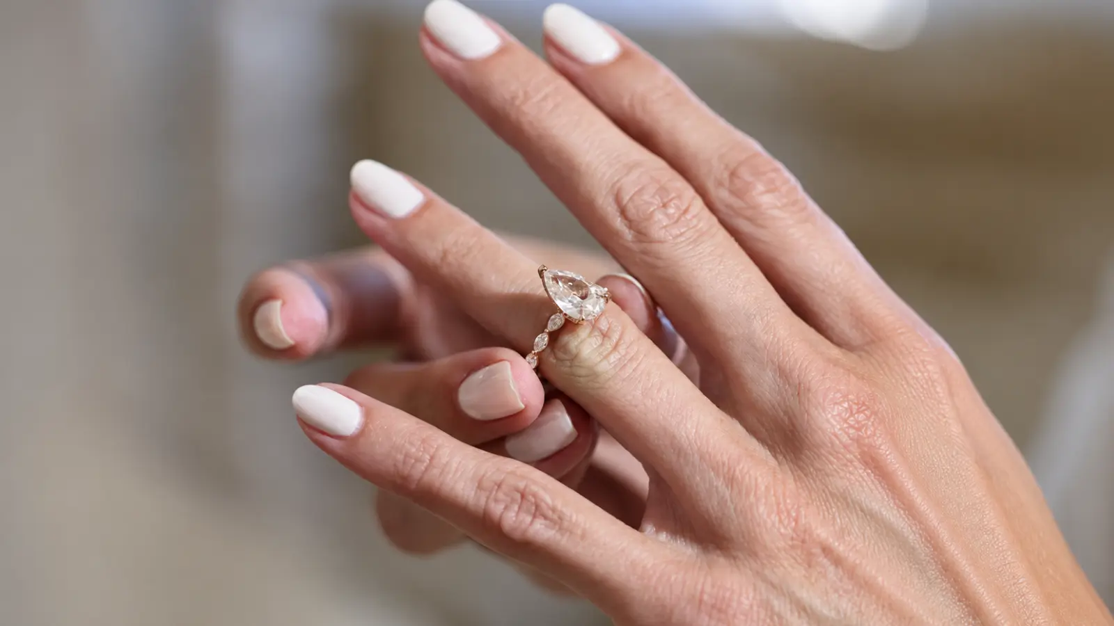 A side view of a pear shaped engagement ring paired with a decorative wedding band on a woman's finger