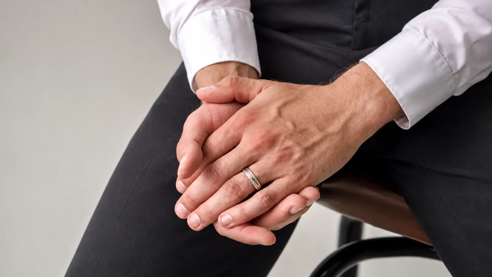 Seated groom wearing a silver and gold two-tone men's wedding band with formal attire, showcasing a versatile mixed-metal wedding ring designed for lasting everyday elegance