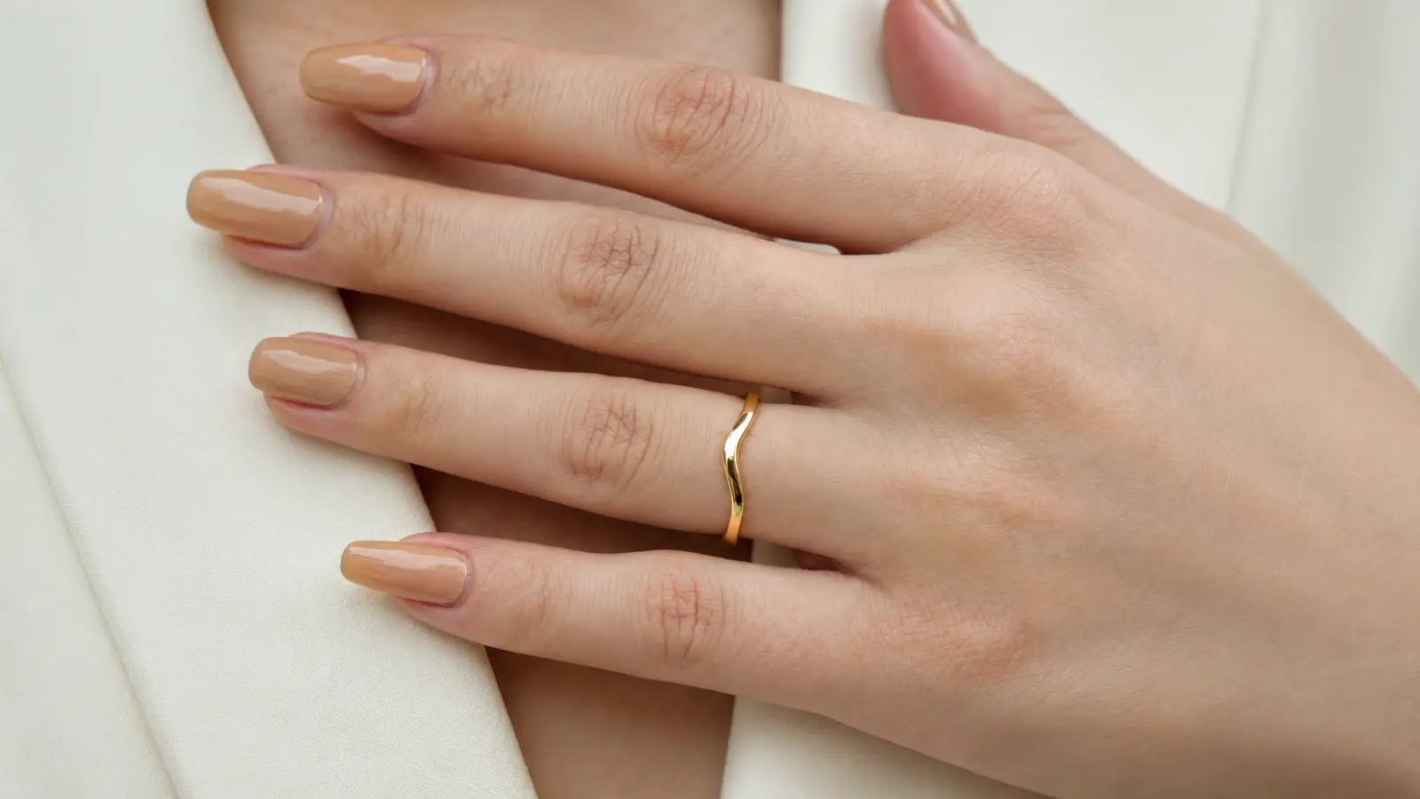 A close-up of a simple curved yellow gold wedding band with a smooth polished finish on a woman's hand