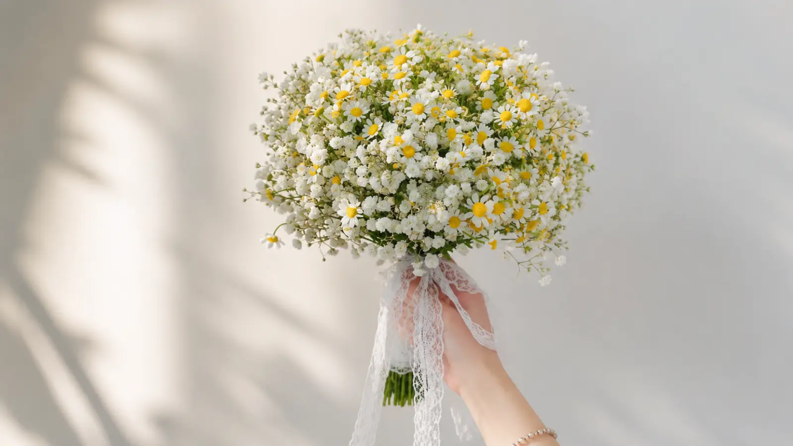 Hand holding a simple DIY wedding bouquet made with small white daisies, baby's breath, and lace ribbon