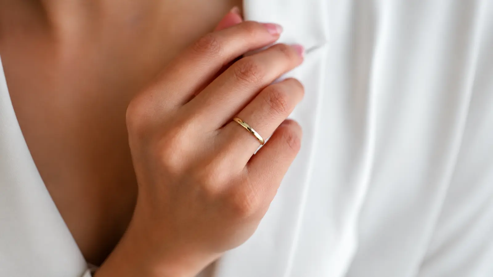 A hand wearing a simple polished gold minimalist wedding band with a smooth finish and understated contemporary style