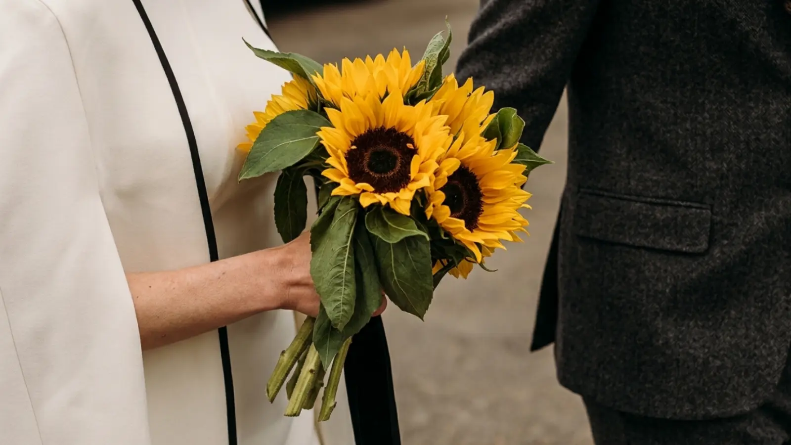 Bride holding a simple sunflower wedding bouquet made with fresh sunflowers and natural green leaves