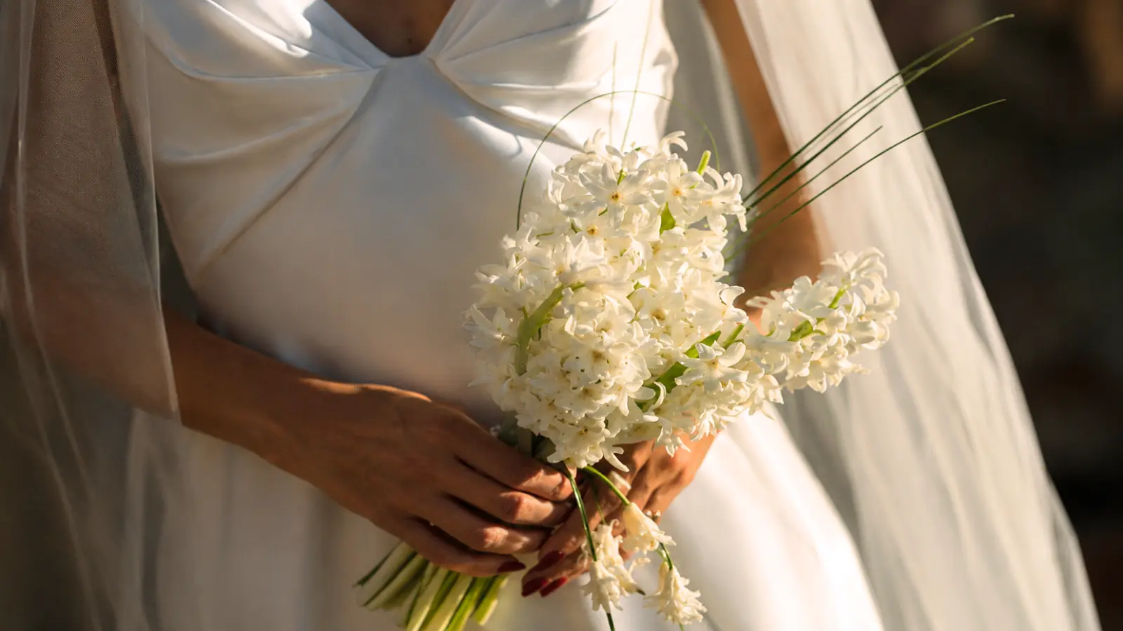 Bride holding a simple white wedding bouquet made with fresh white flowers and long green stems during golden hour