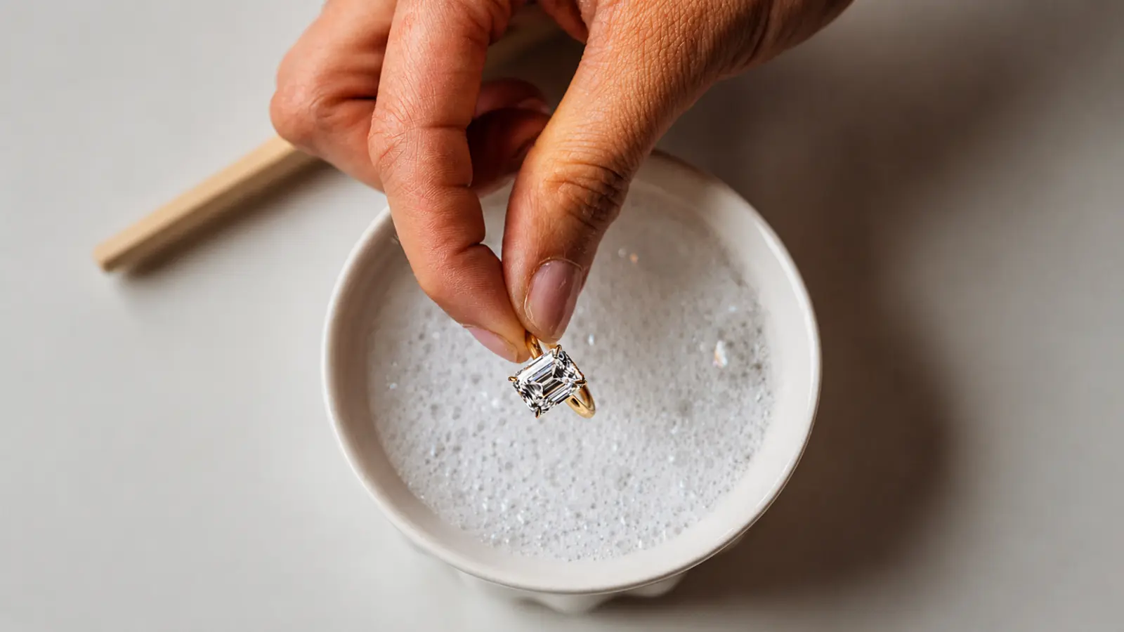 A gold engagement ring soaking in warm soapy water as the first step of safe at-home jewelry cleaning How to Clean a Wedding Ring at Home Safely